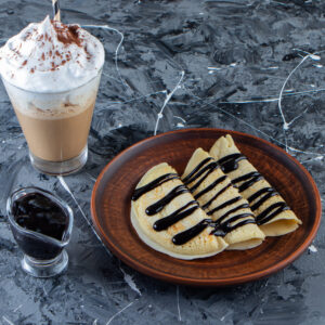 plate of homemade crepes with chocolate topping and glass of coffee